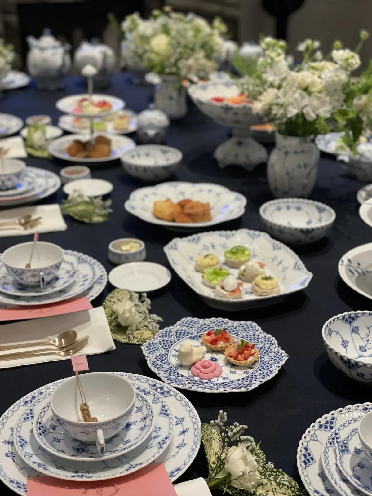 긴 연회 테이블 위에 여러 개인 자리세팅과 카나페 접시가 나란히 놓인 와이드샷