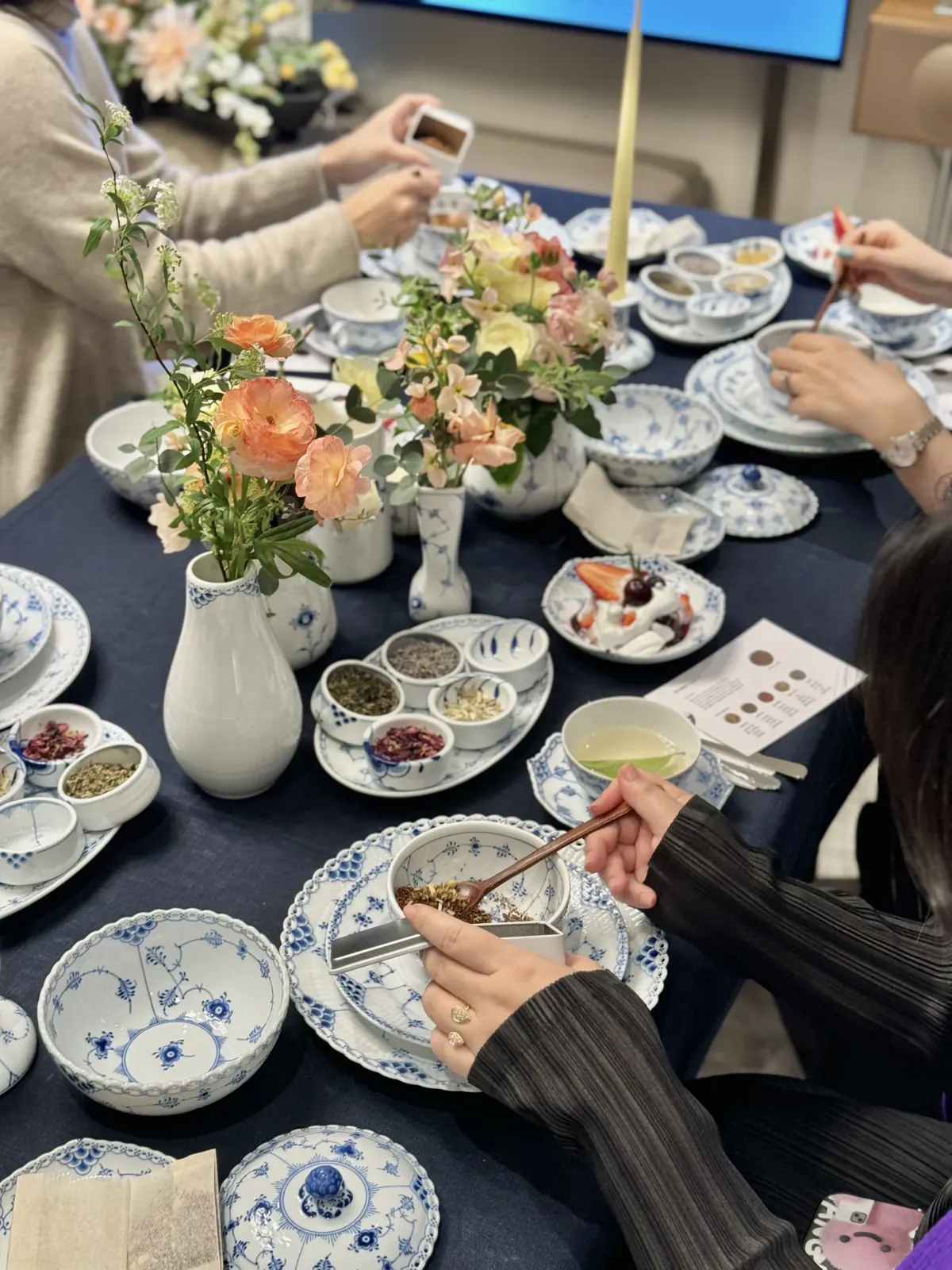 푸른 무늬 식기와 생화 장식 사이에서 참가자가 블렌딩 재료를 스푼으로 담는 모습