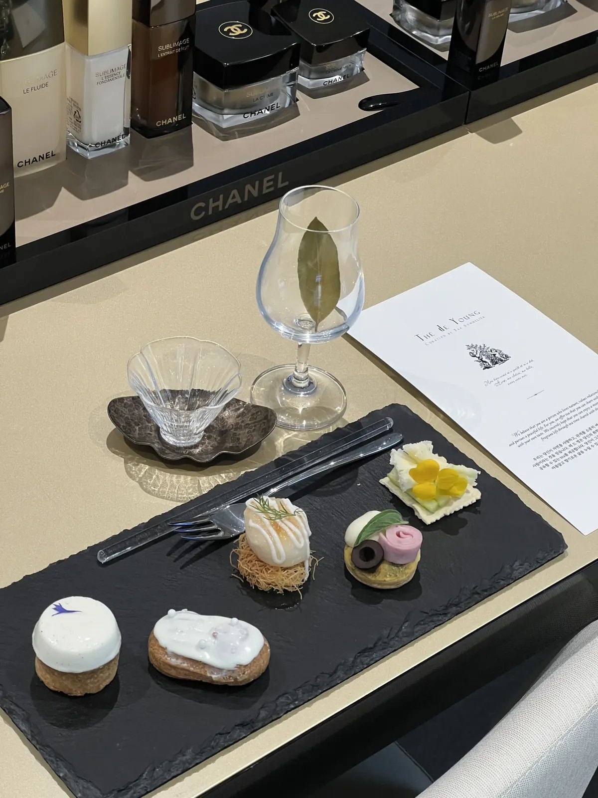 CHANEL 제품 진열대 앞, THE de YOUNG 카드가 선명히 보이는 슬레이트 트레이 프티푸르 세팅
