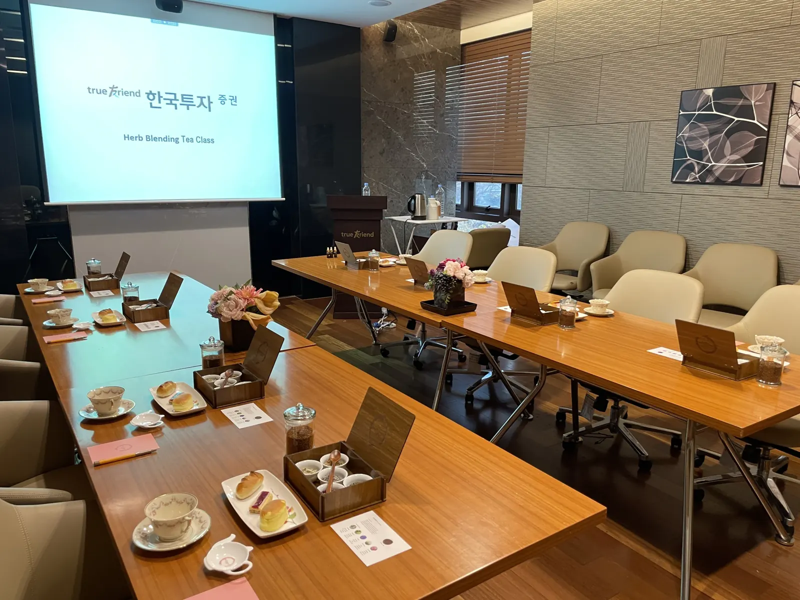 회의실 광각샷, 다수 좌석과 블렌딩 박스, 스크린 슬라이드가 함께 보이는 행사 현장